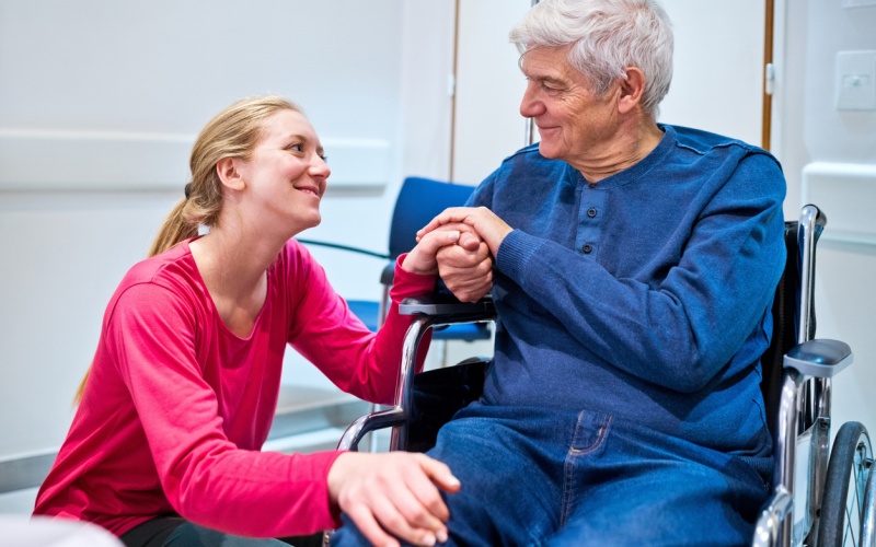 stock photo capturing the essence of attendant care in workman’s compensation cases, a radiant granddaughter looks up proudly at her wheelchair-bound grandfather, illustrating how to navigate challenges when the road gets rough