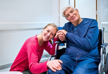 In a stock photo of grinning granddaughter beside wheelchair-bound grandfather in stock photo illustrates Attendant Care in Workers’ Compensation Cases